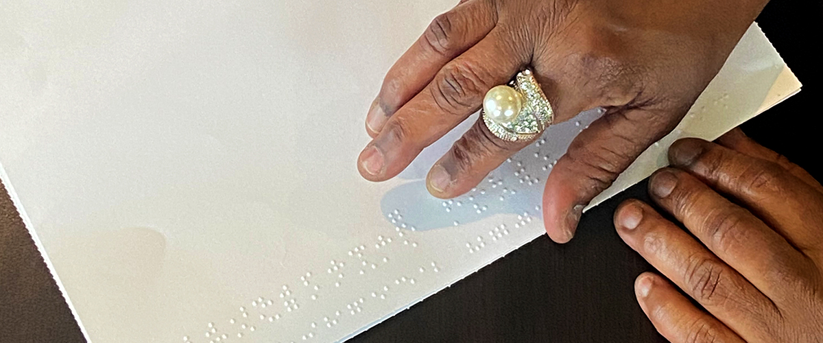 A person's hands reading a piece of paper with braille on it.